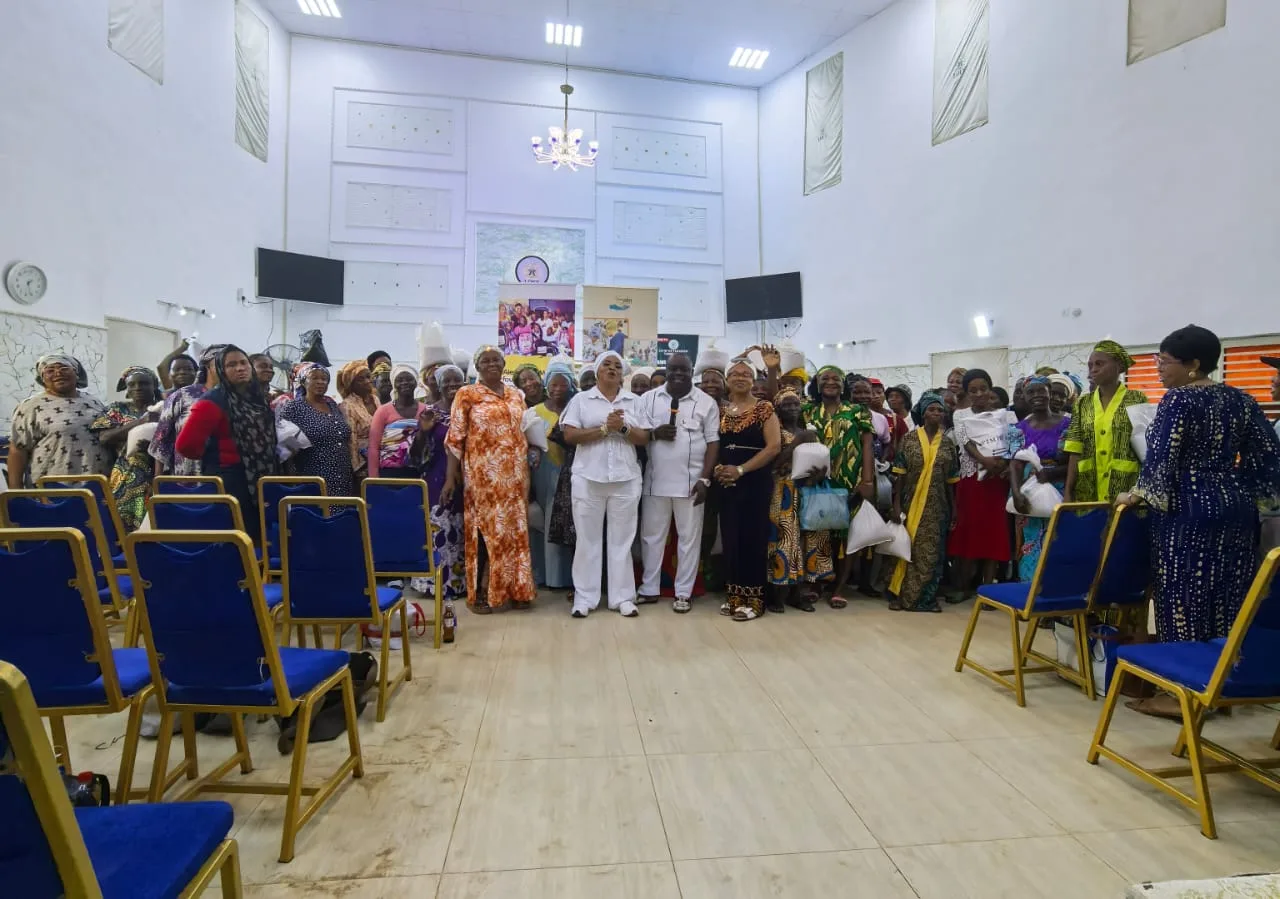 A hall full of older women gathered with the Foundation team at an outreach, holding bags of food.